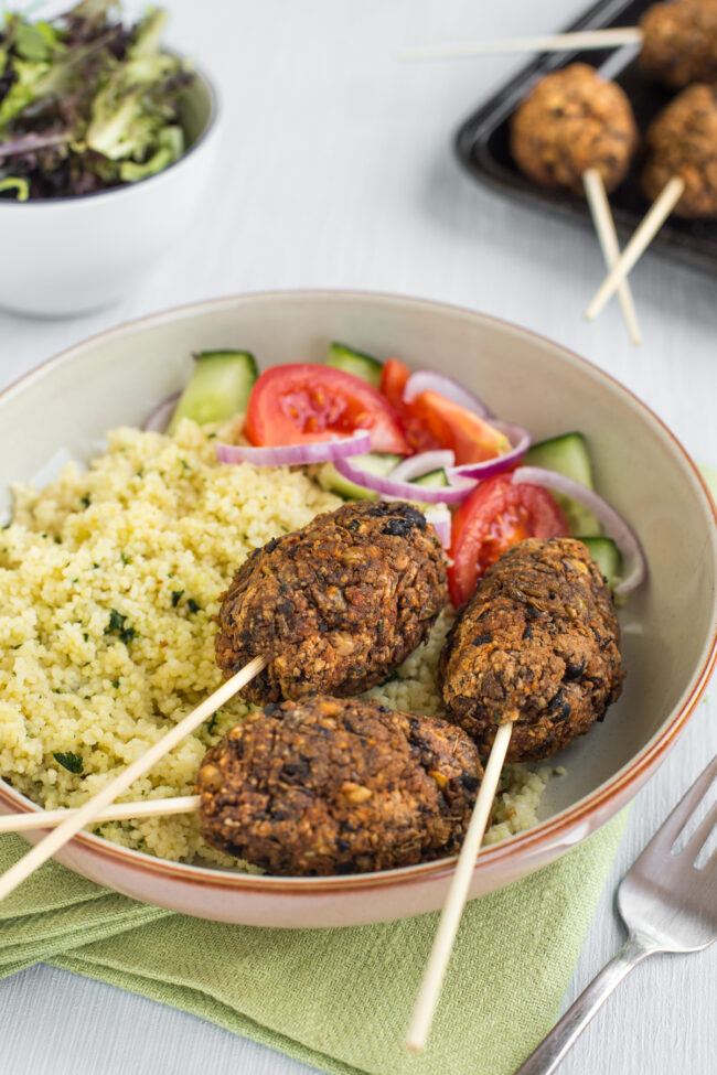 Vegetarian koftas on skewers, served in a bowl with couscous and tomato salad.