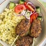 Vegetarian lentil koftas in a bowl, served with couscous and a simple tomato salad.