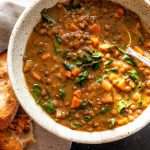 Homemade lentil soup with kale, carrots and tomato paste in a bowl with a spoon.