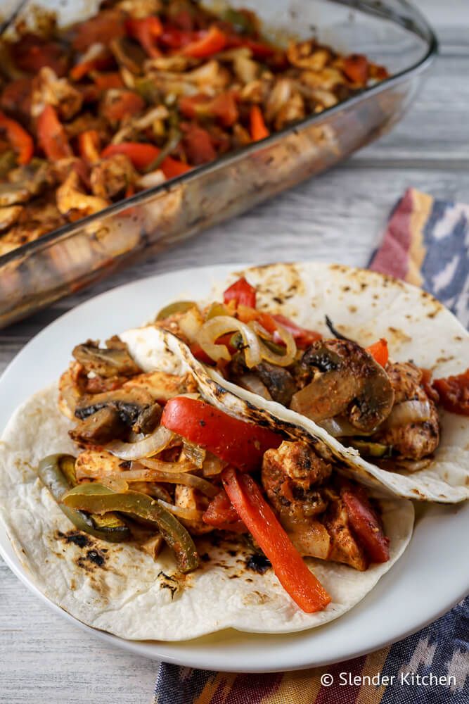 Chicken fajitas that are baked in a glass pan with spices, peppers, onions, tomatoes, and mushrooms.