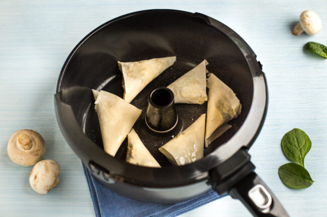 Uncooked homemade samosas in a Tefal Actifry pan.