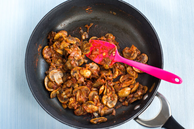 Rich tomatoey mushrooms cooking in a frying pan.