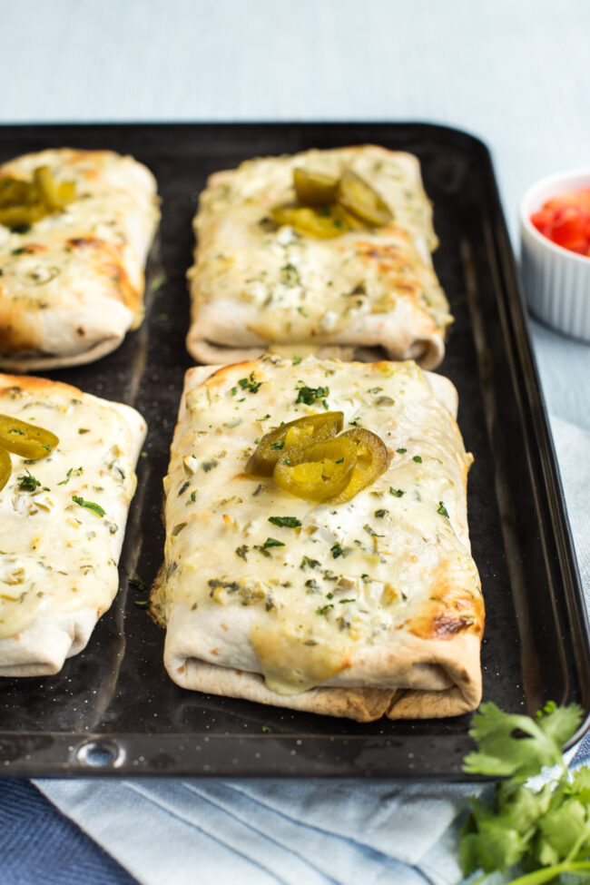 Vegetarian smothered burritos topped with jalapenos on a baking tray.