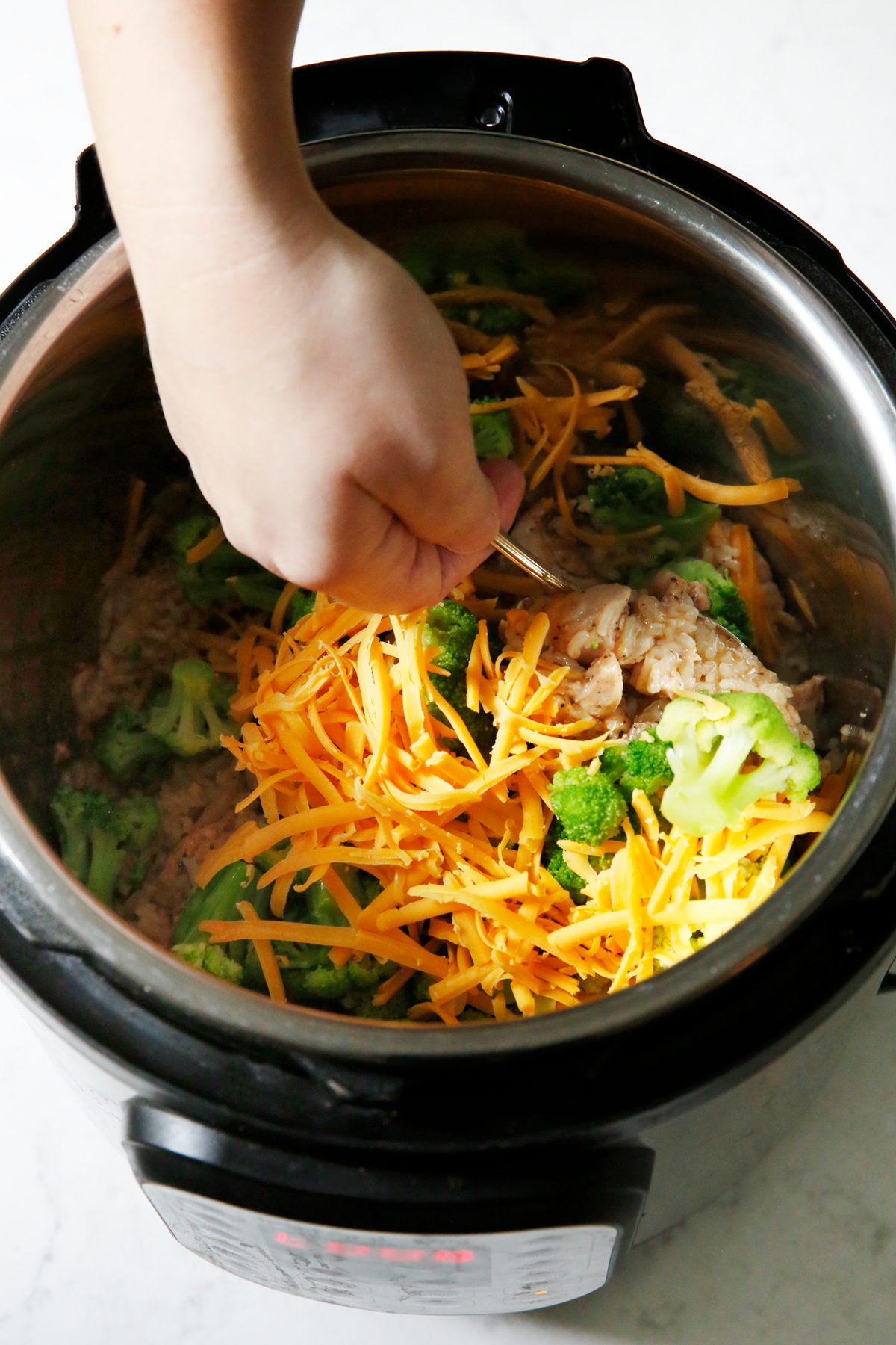 Stirring cheese into the instant pot with chicken broccoli and rice