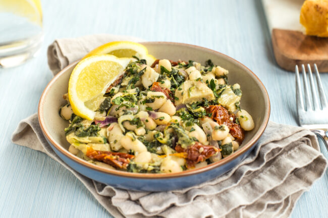 Portion of Tuscan beans in a blue bowl with spinach and sun-dried tomatoes.