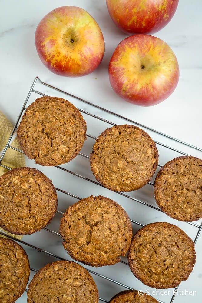 Applesauce muffins with oatmeal on a baking rack with apples on the side.