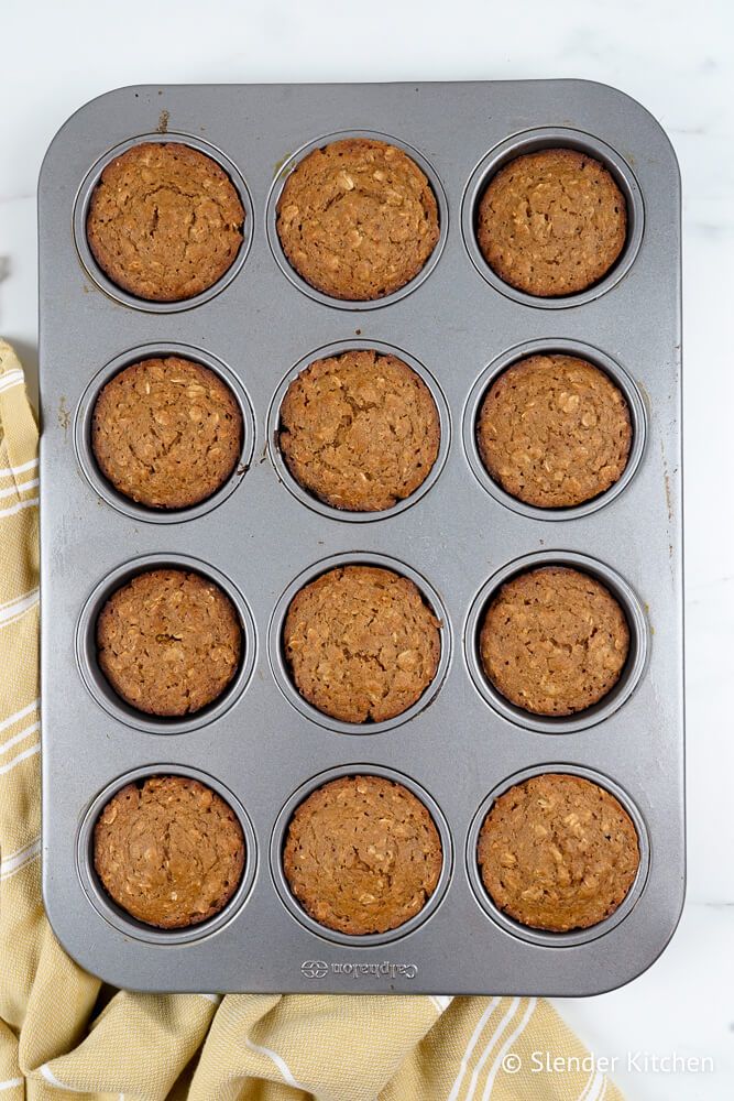 Oatmeal muffins with applesauce in a muffin tin with lightly browned tops.