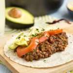 A lentil and quinoa taco topped with sliced tomatoes and avocado.