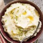 Crockpot Mashed Potatoes Recipe potatoes in a bowl with butter and chives and a spoon in it