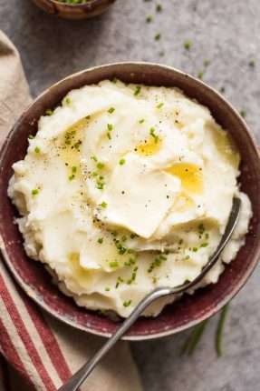 Crockpot Mashed Potatoes Recipe potatoes in a bowl with butter and chives and a spoon in it