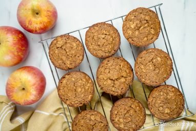 Applesauce oatmeal muffins with oatmeal flecks on a baking rack with a yellow napkin and apples.