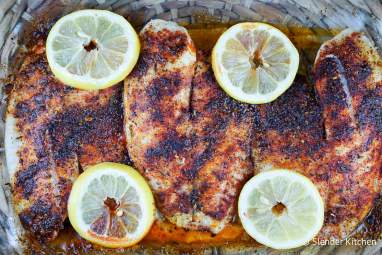 Blackened tilapia in a glass baking dish with lemon slices and blackening seasoning.