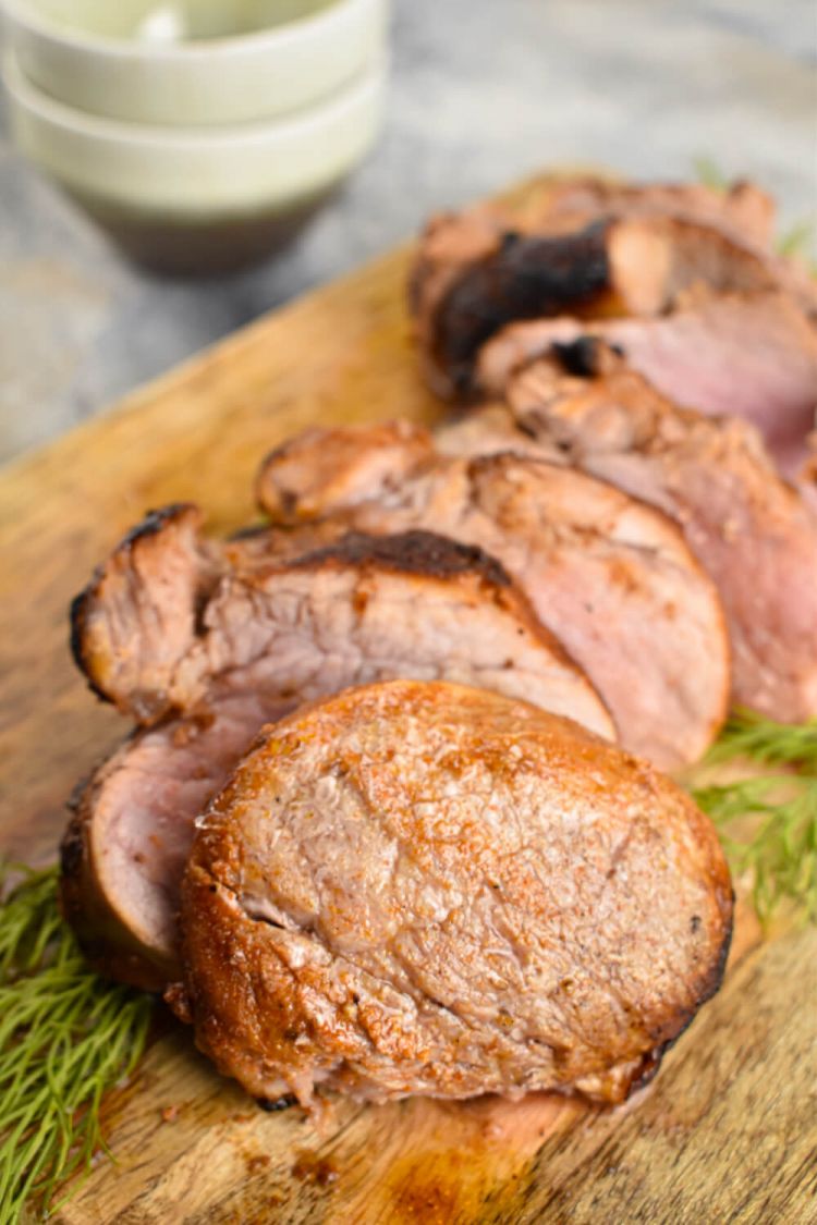 Pork tenderloin with a spice rub sliced on a cutting board.