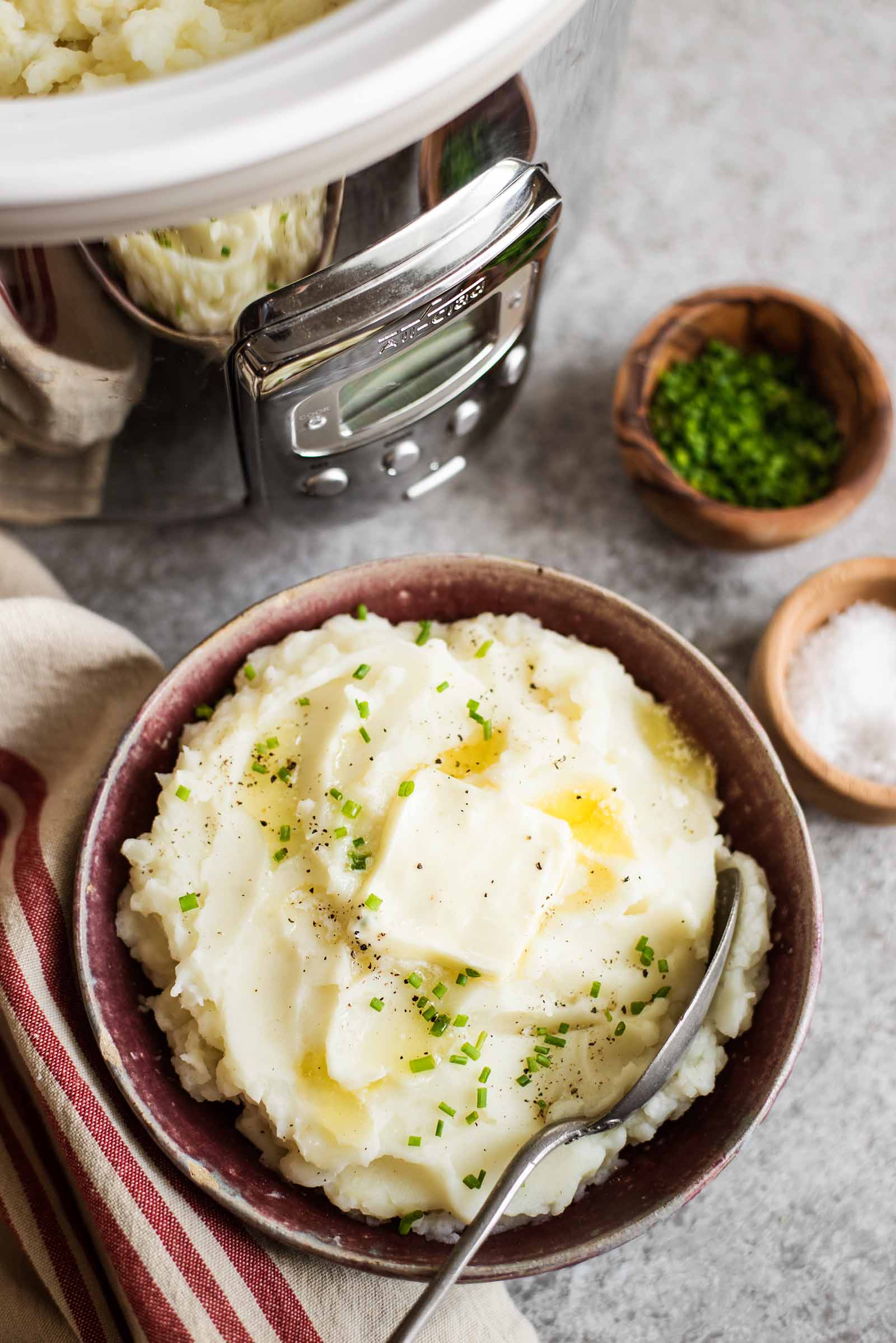 Slow Cooker Mashed Potatoes in serving dish with slab of butter and chives