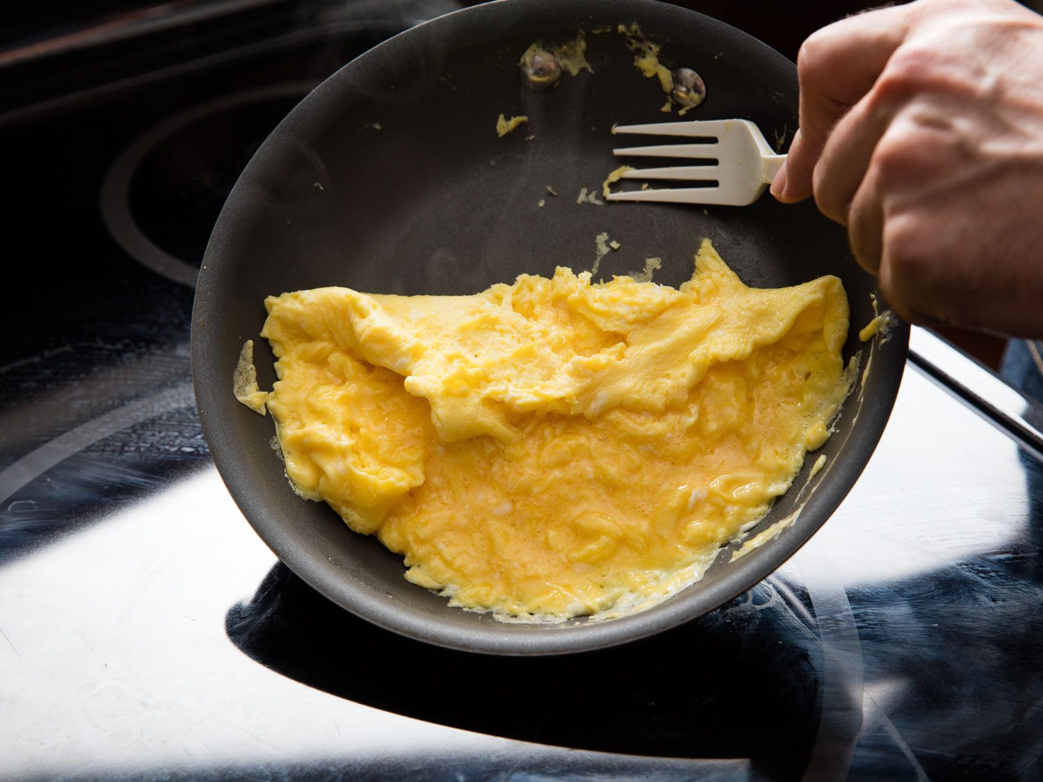 Using a plastic fork to scrape large curds of scrambled eggs toward the center of a nonstick skillet