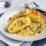 A cheesy mashed potato cake on a plate, cut in half to reveal a creamy mushroom filling.