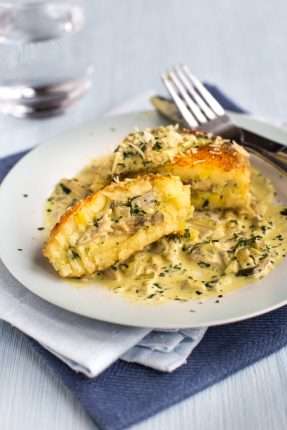 A cheesy mashed potato cake on a plate, cut in half to reveal a creamy mushroom filling.