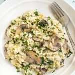 Portion of creamy spinach and mushroom risotto in a bowl with a fork.