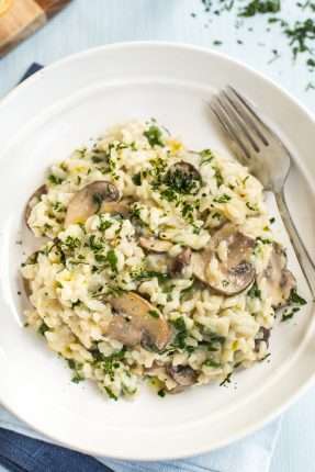 Portion of creamy spinach and mushroom risotto in a bowl with a fork.