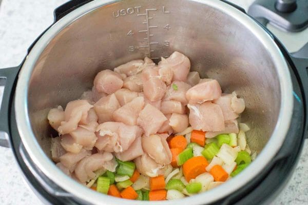 Raw chicken diced up with vegetables in an instant pot.