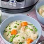 A blue bowl on a pink cloth filled with chicken and dumplings with an instant pot in the background.