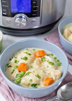 A blue bowl on a pink cloth filled with chicken and dumplings with an instant pot in the background.