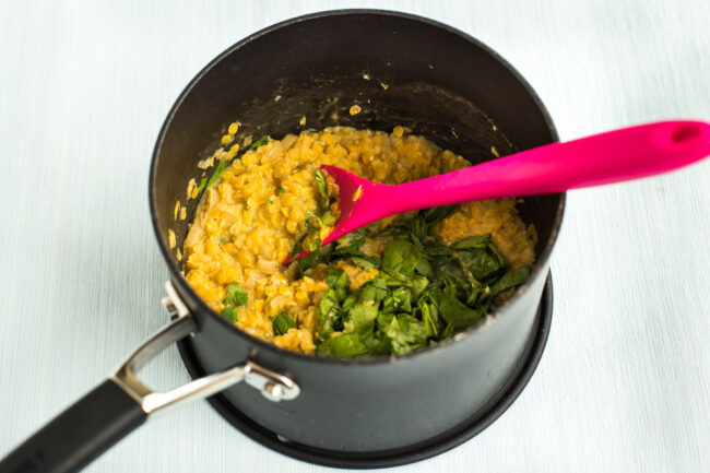Cooked red lentils in a saucepan with fresh spinach.