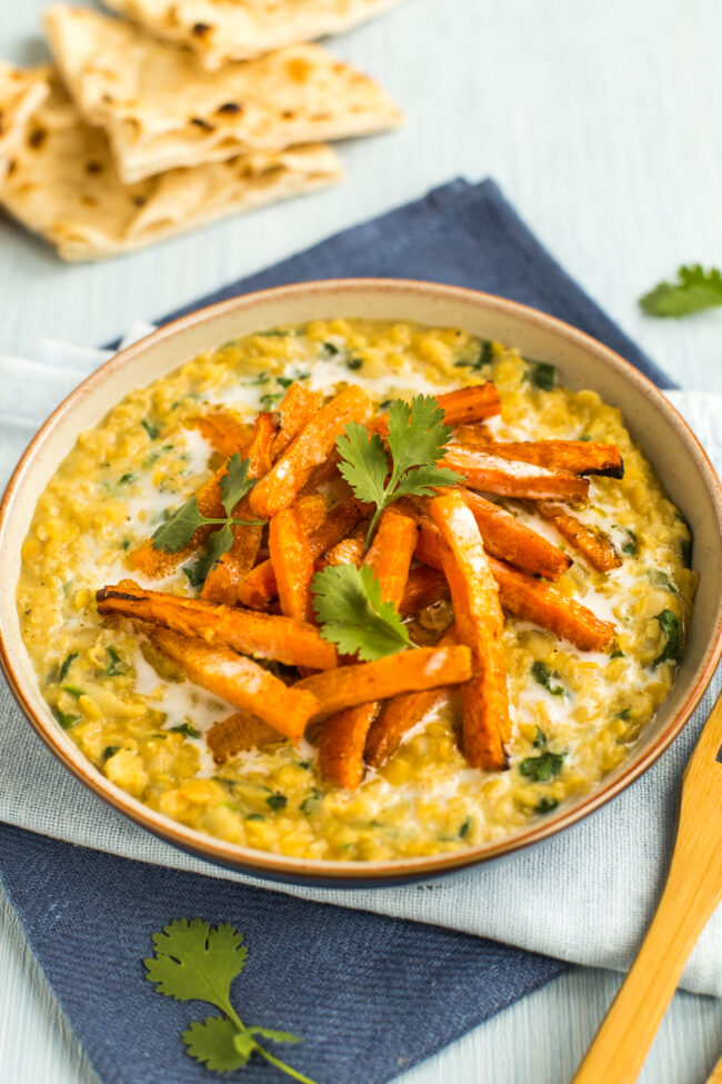 Portion of creamy lentil dal in a bowl topped with roasted carrots, coconut milk and cilantro.