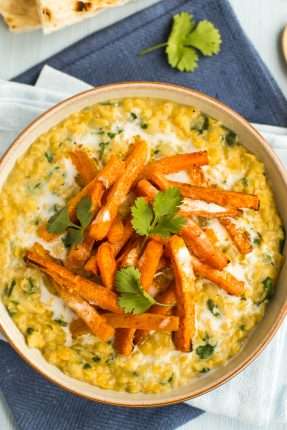 Portion of creamy lentil dal in a bowl topped with roasted carrots and cilantro.