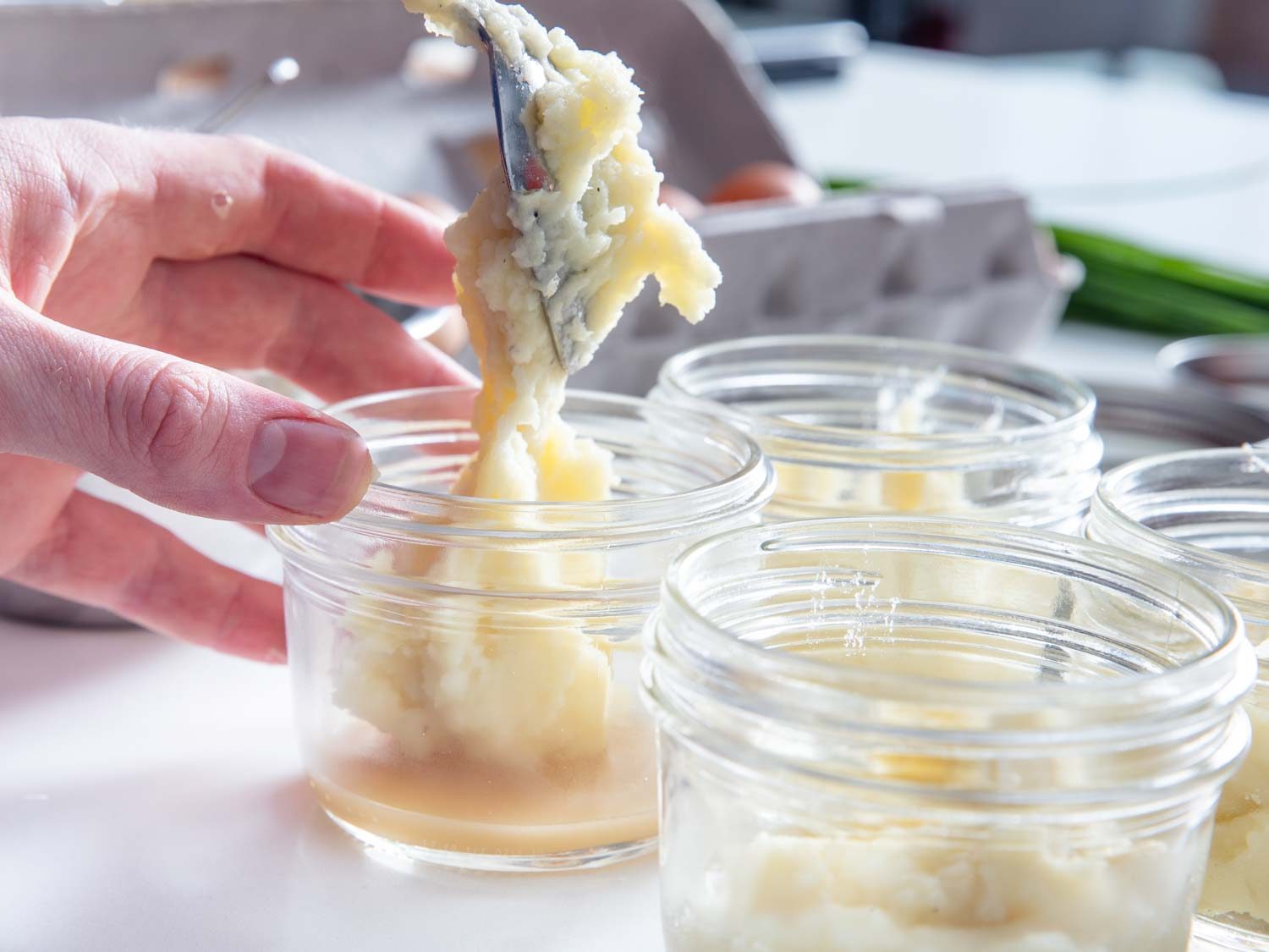 Spooning mashed potatoes over gravy in a Mason jar.