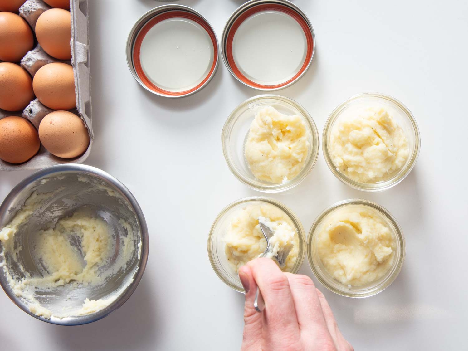 Overhead of dividing mashed potatoes between four Mason jars.