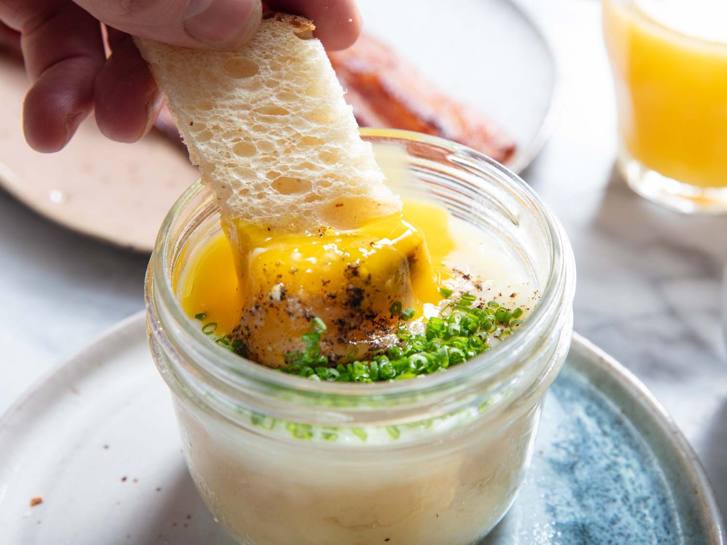 Closeup side view of toast being dipped into a potato-egg jar, breaking the custardy egg yolk.