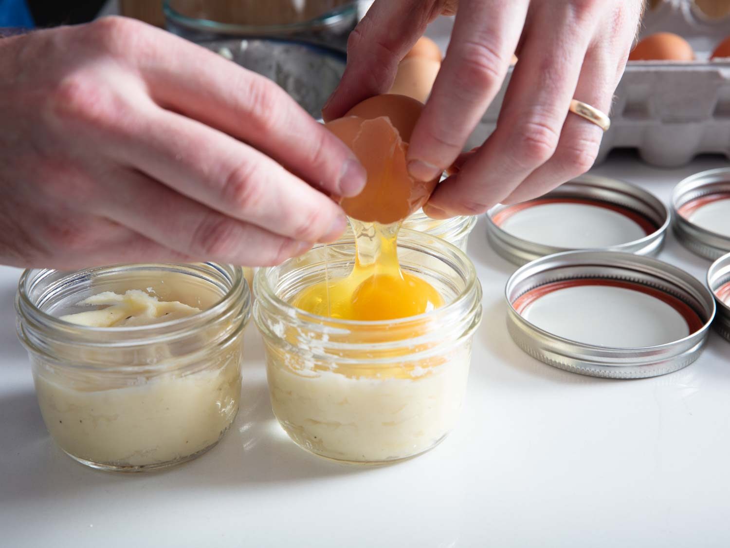Cracking an egg into a Mason jar with mashed potatoes.