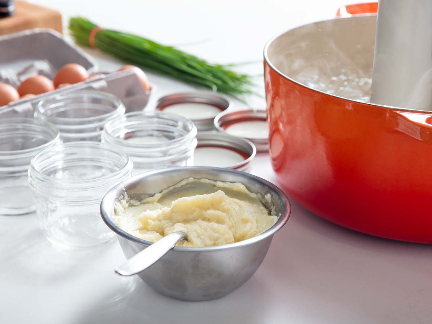 A bowl of mashed potatoes next to a sous vide water bath and Mason jars.