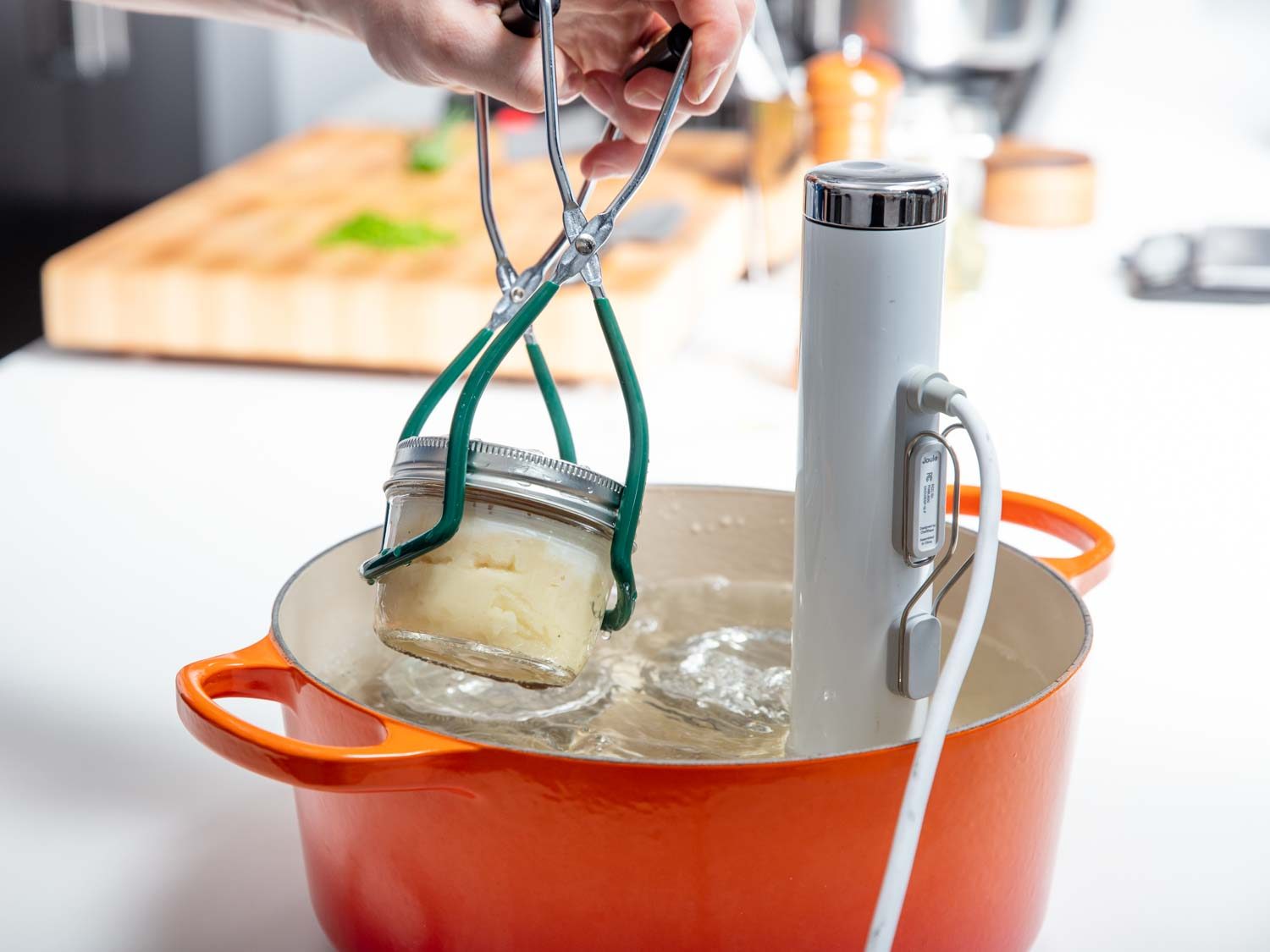 Pulling a Mason jar out of the sous vide bath with a pair of canning tongs.