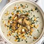 Portion of vegan cream of mushroom soup topped with fried mushrooms and pine nuts.