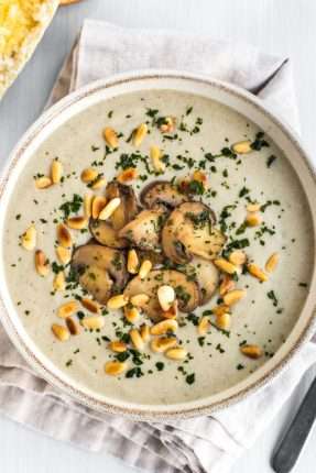 Portion of vegan cream of mushroom soup topped with fried mushrooms and pine nuts.