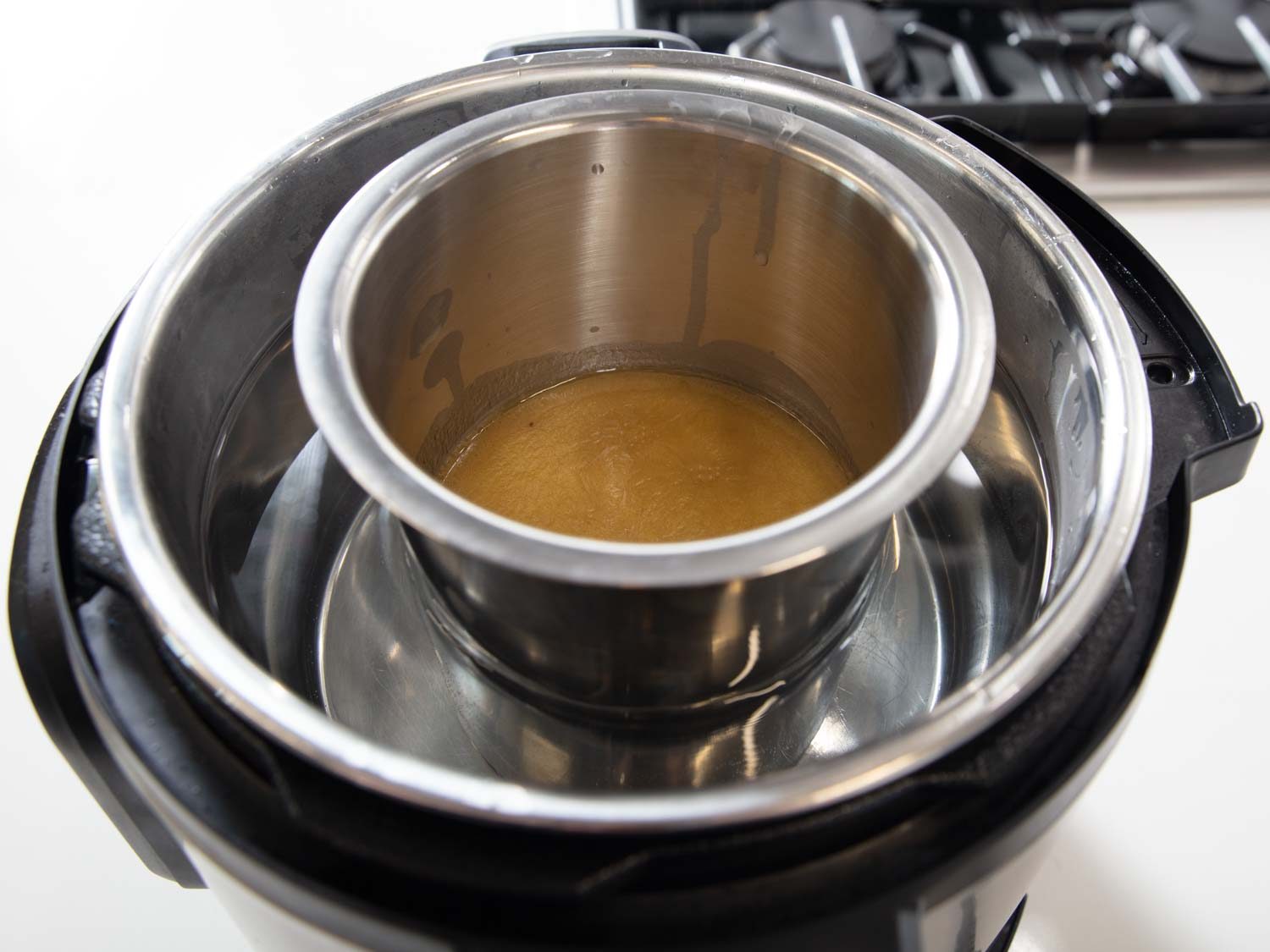 Here, a metal container holding gravy is sitting in a hot-water bath created using a multi-cooker set on its slow-cooker setting