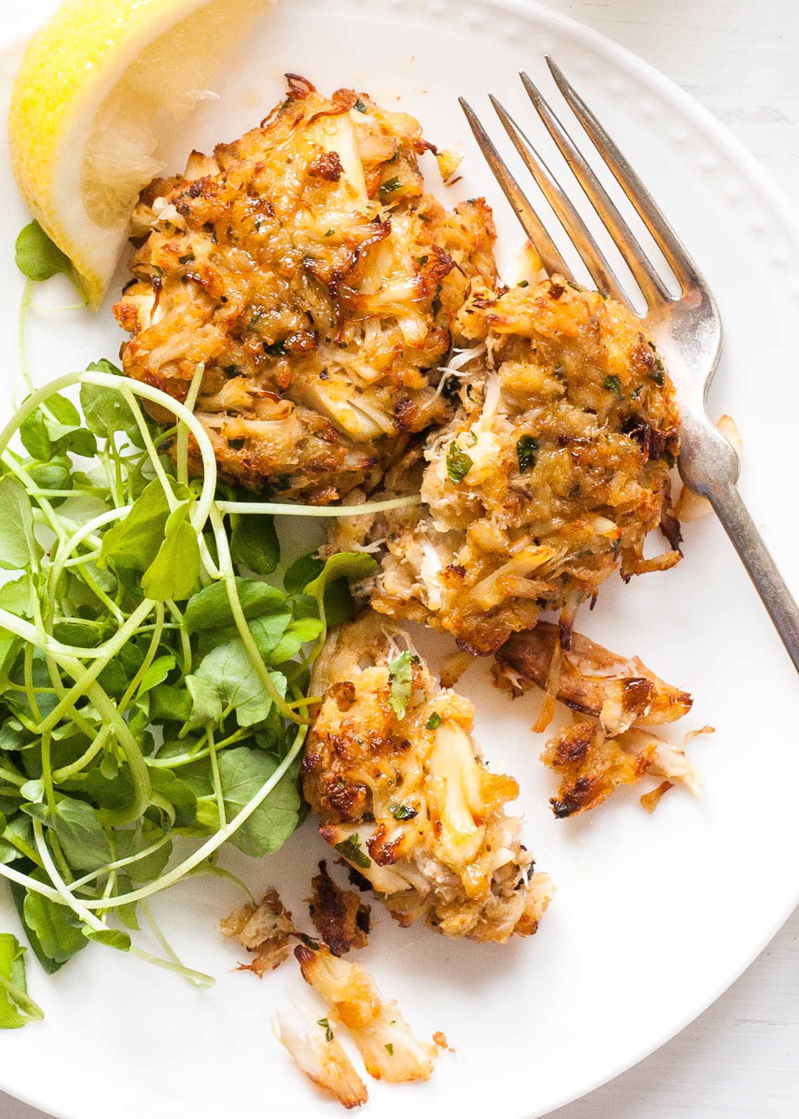 Maryland Crabcakes wtih greens and lemon wedges on a white plate wtih mayo