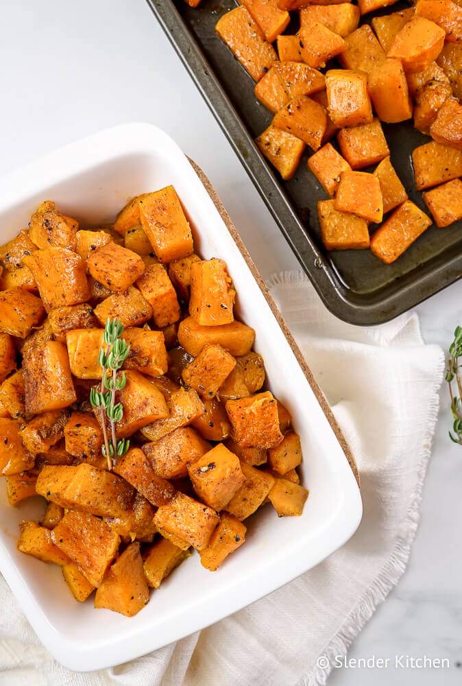 Roasted cinnamon butternut squash in a dish with fresh thyme and on a baking sheet.