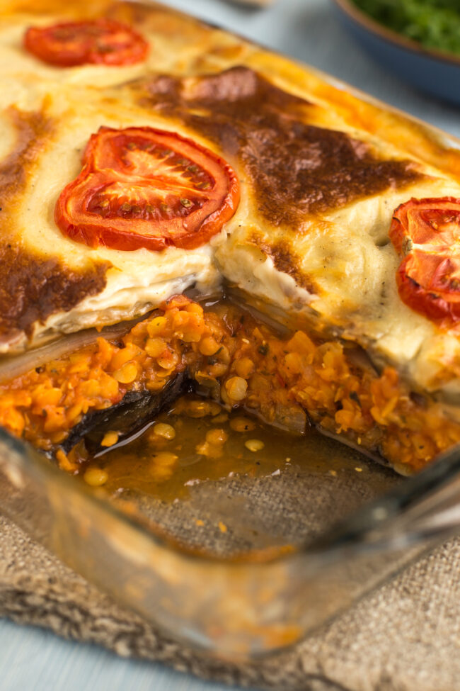A vegetarian moussaka in a baking dish with a portion removed.