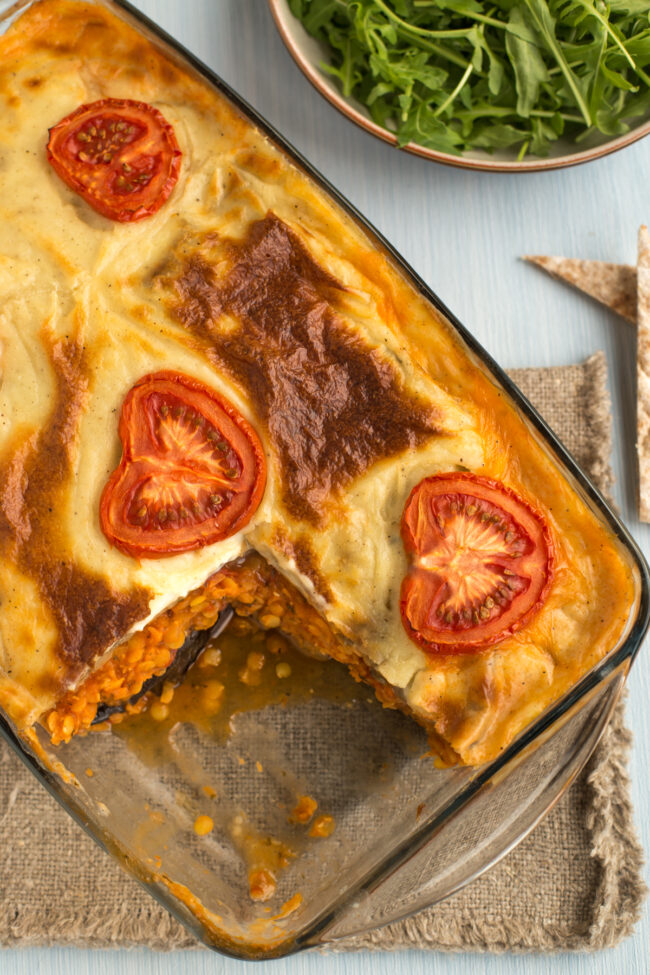 A baked vegetarian moussaka topped with sliced tomatoes, with a portion removed.
