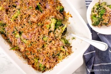 Healthy broccoli casserole with mushrooms, cheddar cheese, and crispy onions in a baking dish with a spoon.