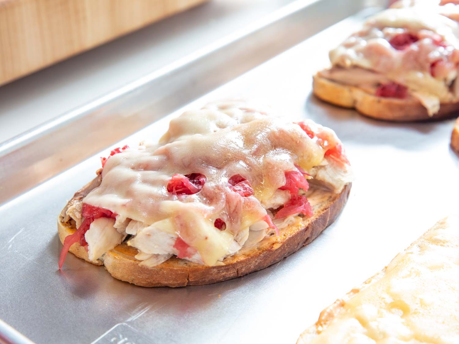 An open-faced turkey Reuben sandwich on a rimmed baking sheet, with melted Swiss cheese.