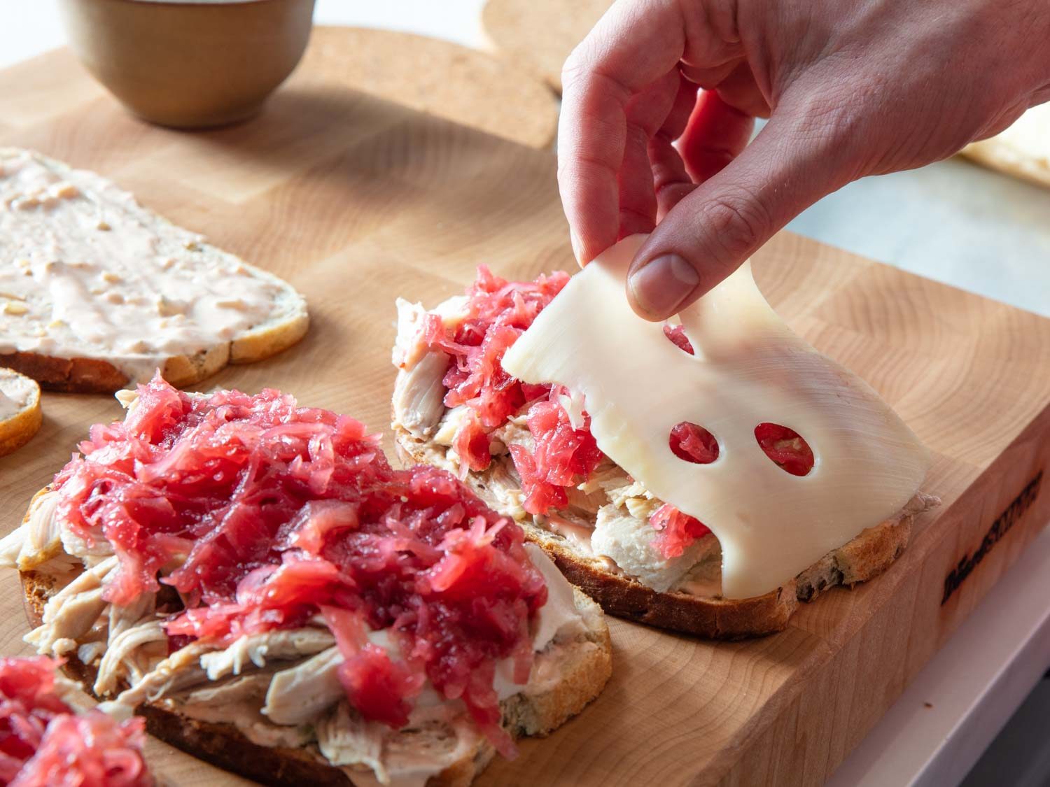 Draping Swiss cheese over a cranberry-sauerkraut while building Reuben sandwiches.