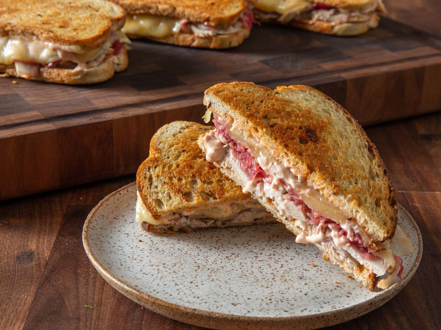 Closeup of a turkey Reuben sandwich on a plate, with more sandwiches on a cutting board in the background.