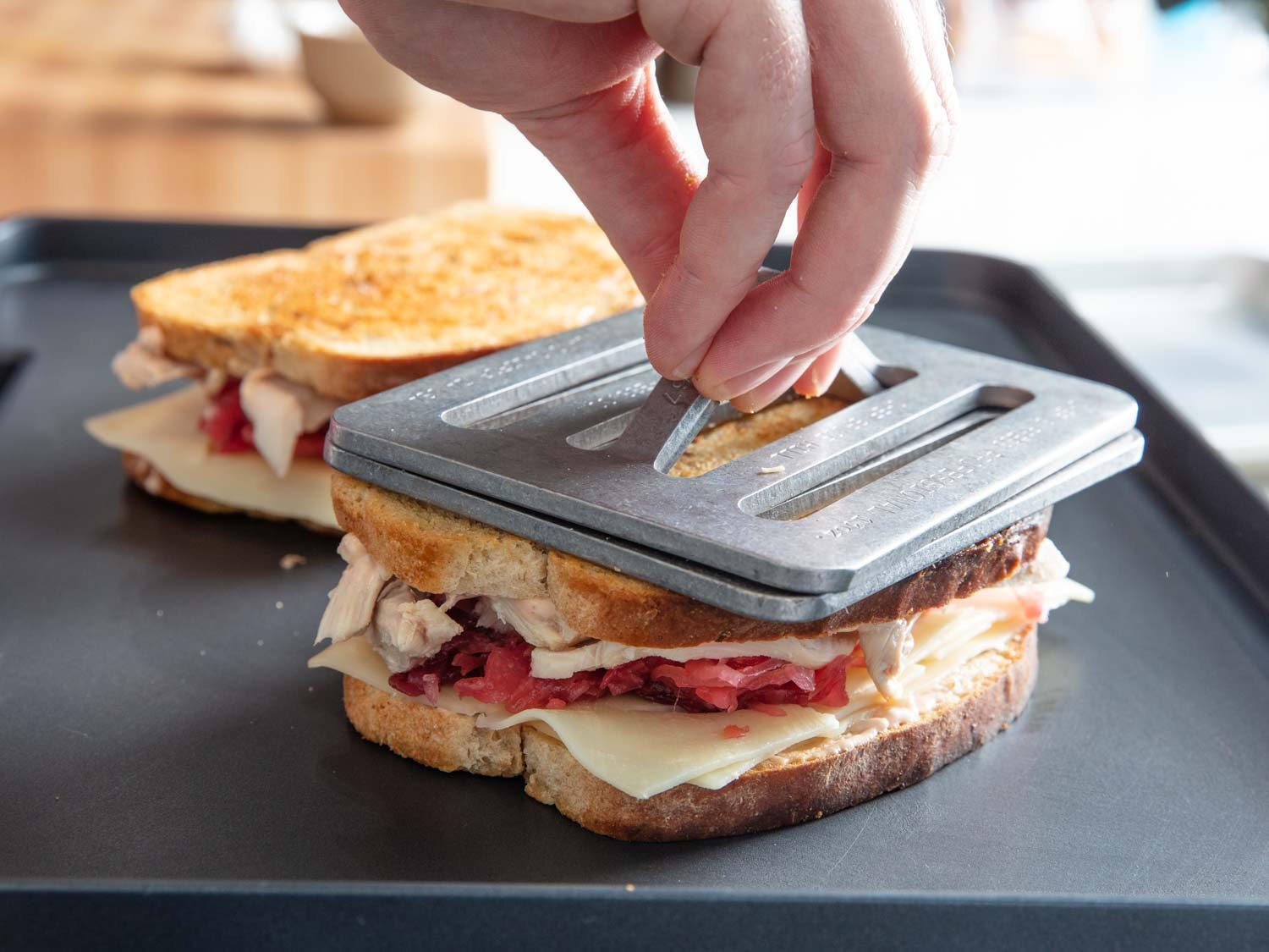 Stacking Chef's Press weights on a turkey Reuben sandwich as it cooks on an electric griddle.