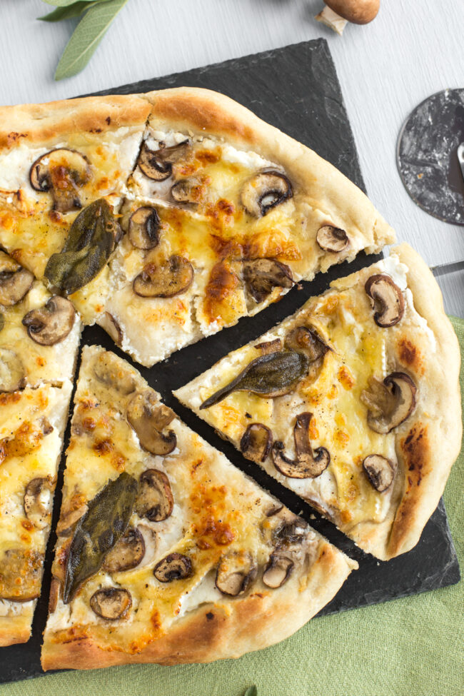 A white pizza topped with mushroom and sage, cut into wonky slices.