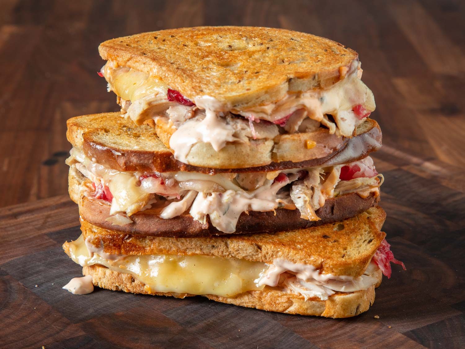 Closeup of a stack of three turkey Reuben sandwiches on a cutting board.